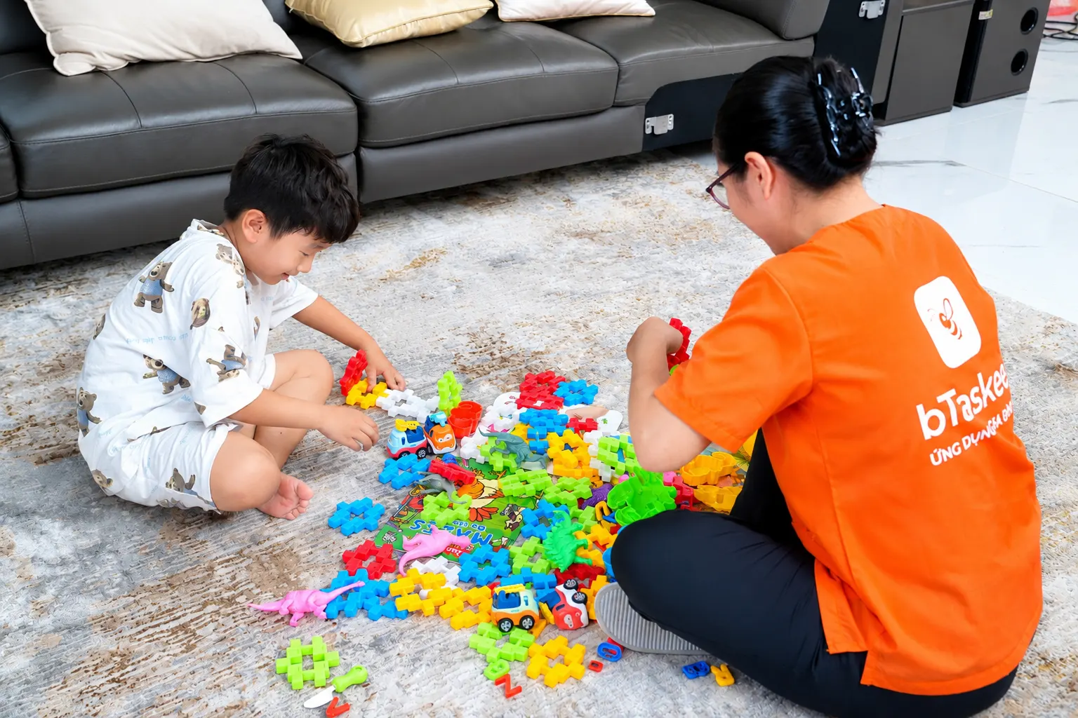 Bảo mẫu chơi xếp hình cùng bé trên thảm phòng khách